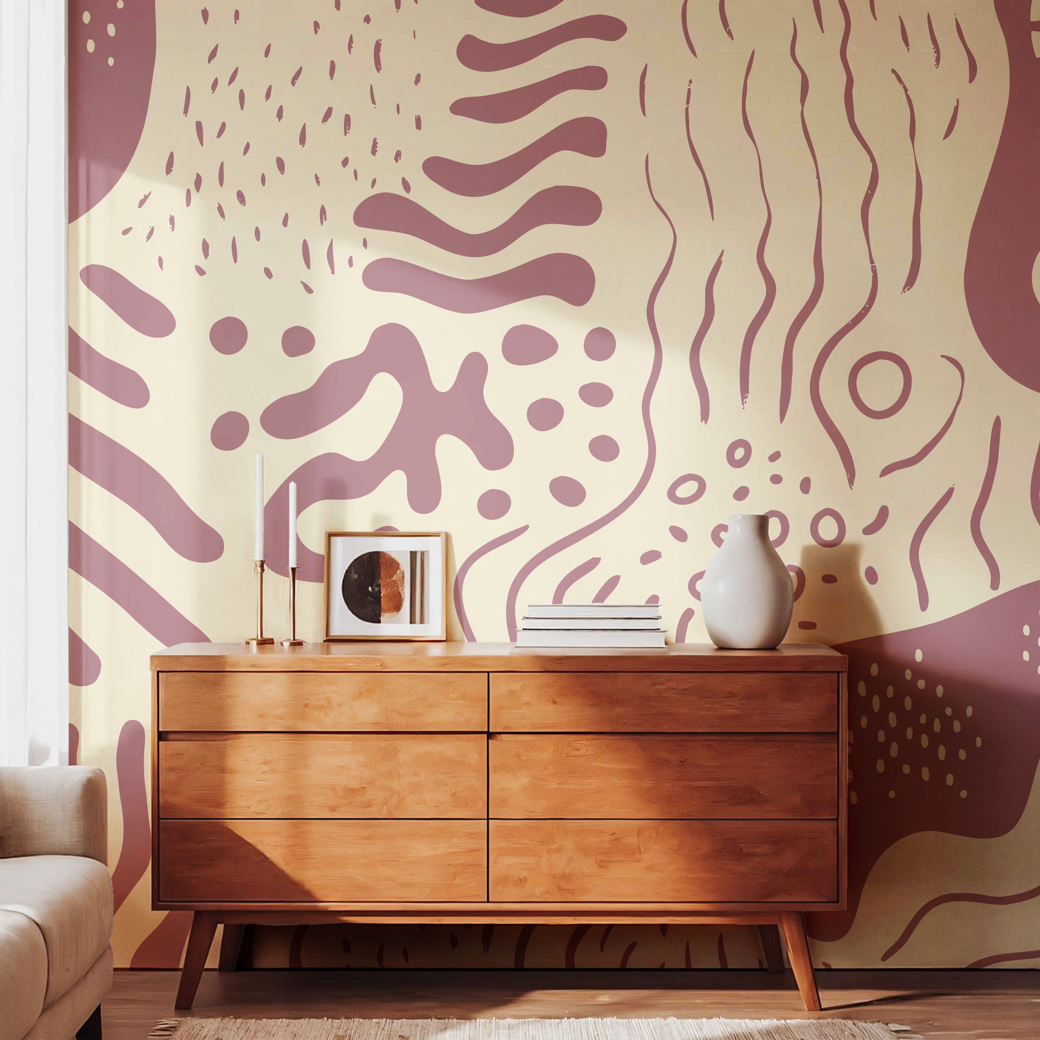 A mid-century modern wooden sideboard or dresser placed against a wall with a repeating floral vine wallpaper pattern. The warm wood cabinet has four drawers and is styled with a framed print, books, and a ceramic vase.