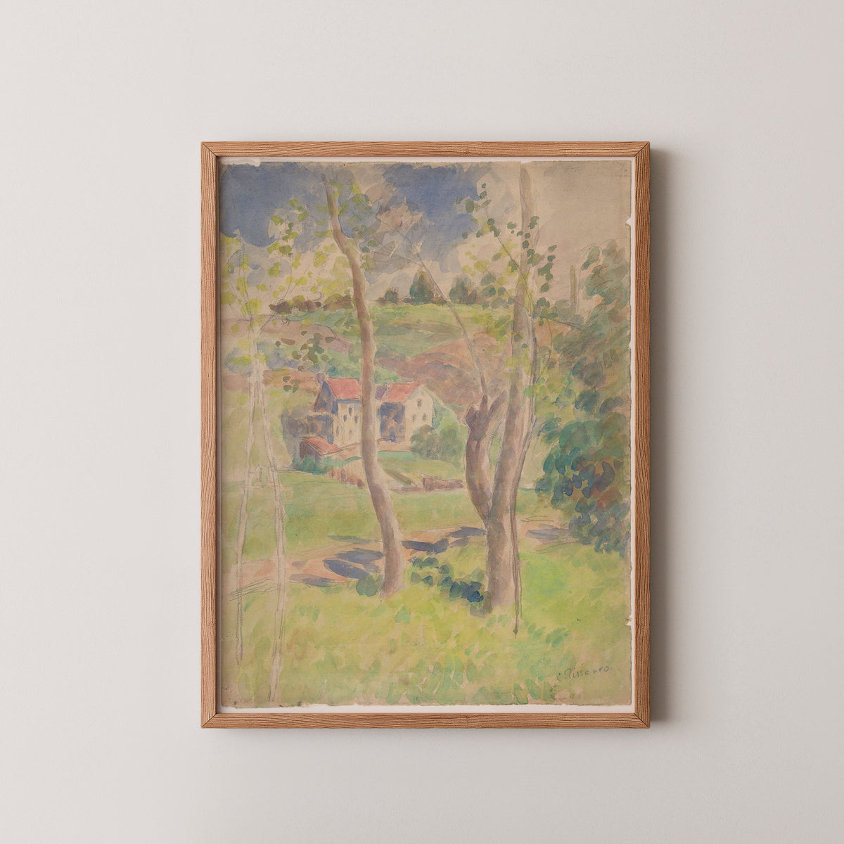Pissarro watercolor art print in a natural wood frame, showing green fields and pale red-roofed houses
