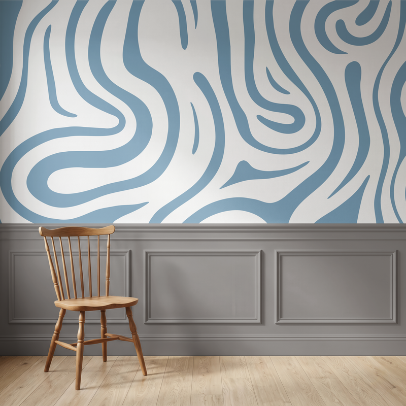 A styled interior scene showing a blue and white wavy abstract wallpaper on the upper wall, gray wainscoting along the lower wall, light wood flooring, and a wooden spindle-back chair in the foreground.