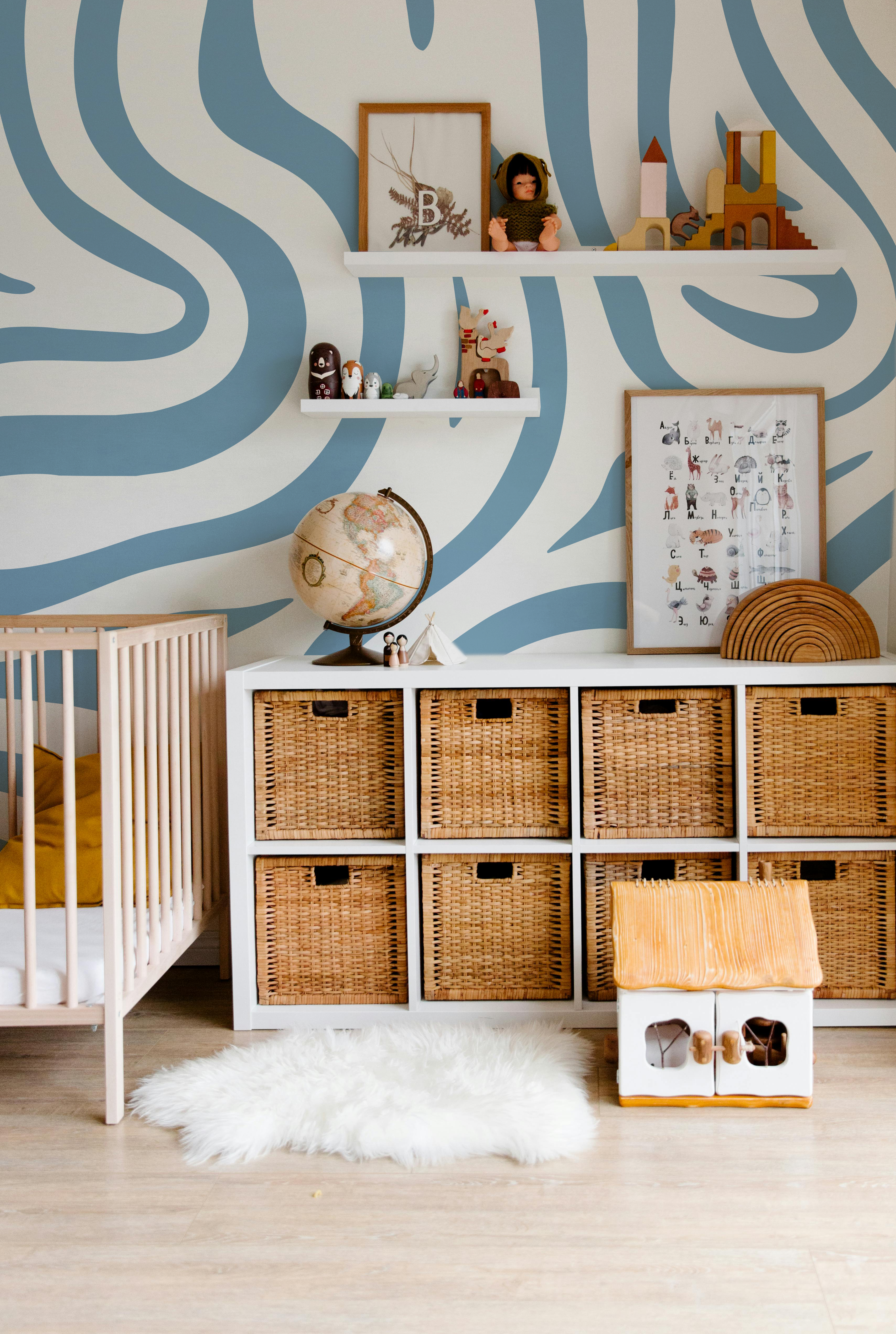 Modern nursery featuring Topo Sky contour wallpaper with soft blue flowing lines, natural wood furniture and woven storage baskets