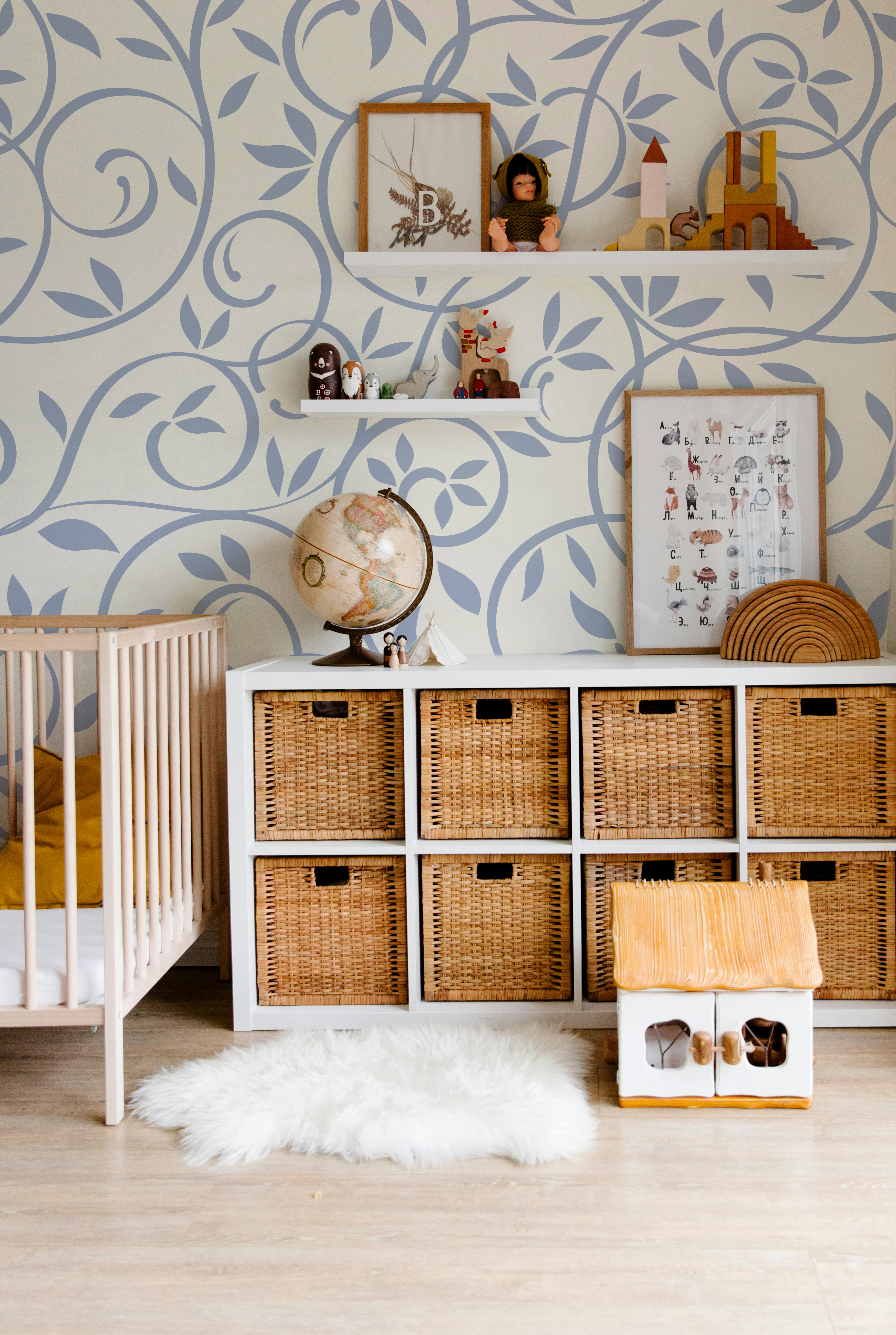 Dusty blue botanical leaf wallpaper styled in a soft modern nursery