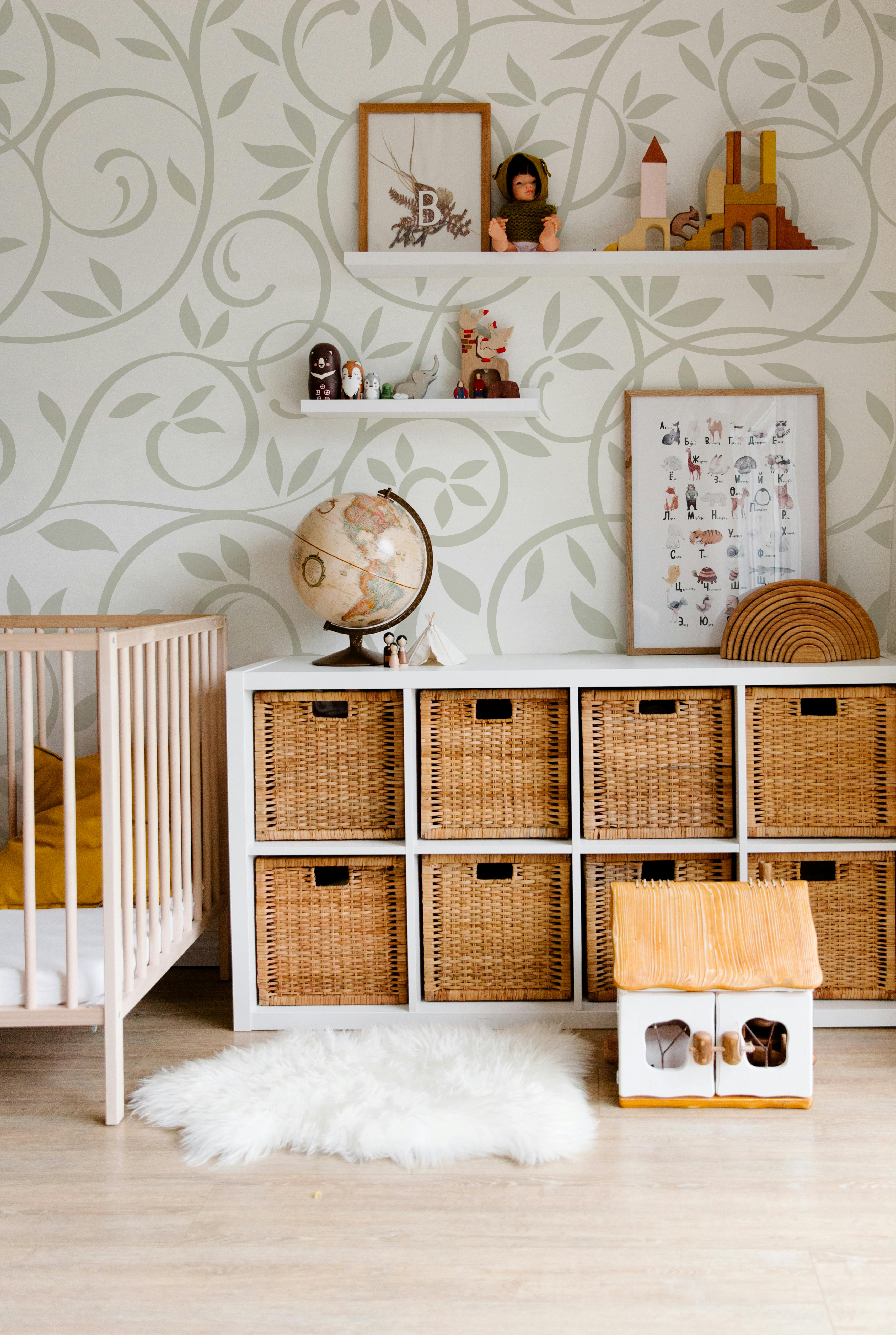 Sage green botanical leaf wallpaper styled in a soft neutral nursery